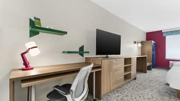 A hotel room with a wooden desk, a TV, a bed, and a chair.