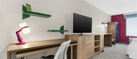 A hotel room with a wooden desk, a TV, a bed, and a chair.