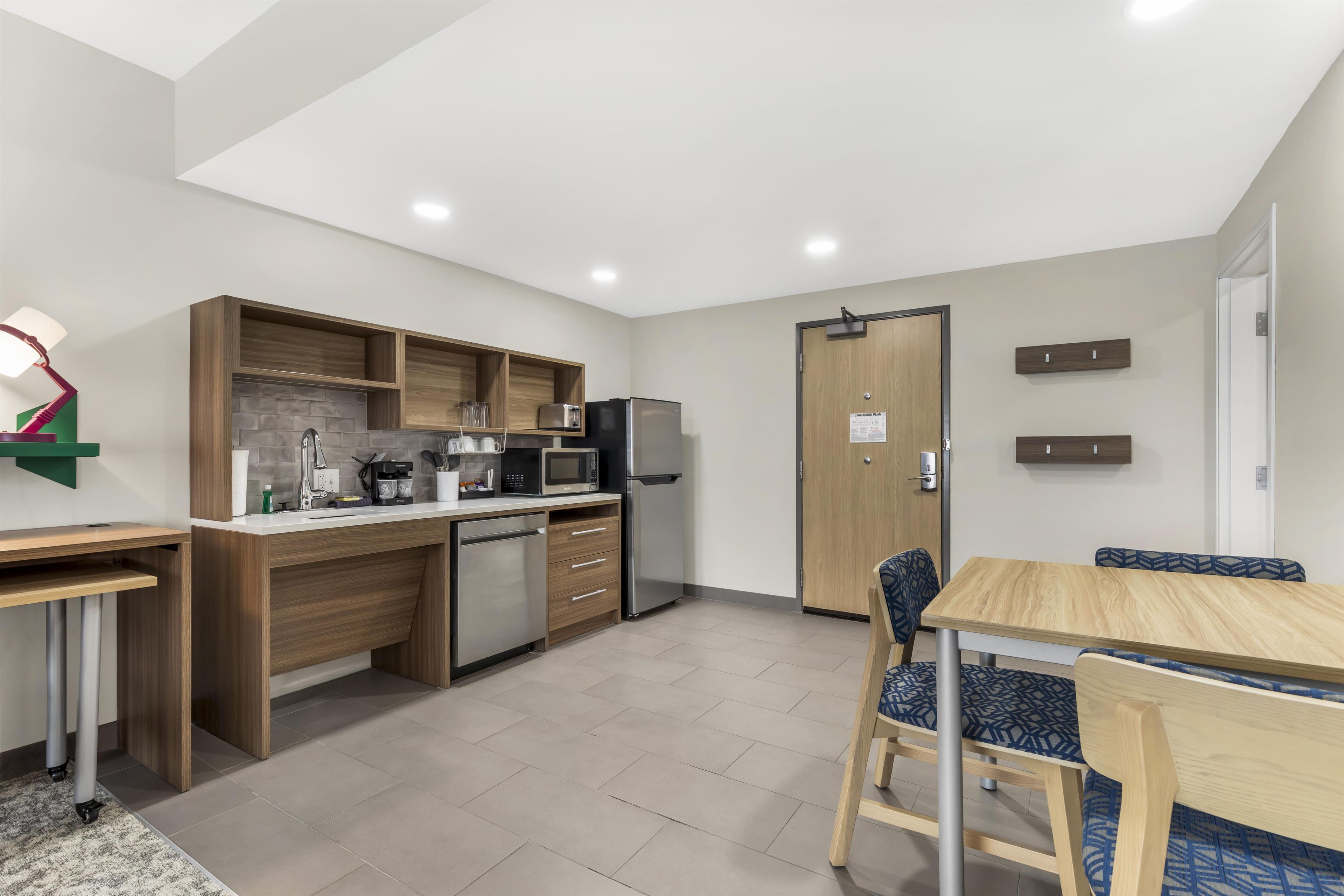 A compact kitchen with modern appliances, a dining area with a table and chairs, and a wooden door with an emergency exit sign.