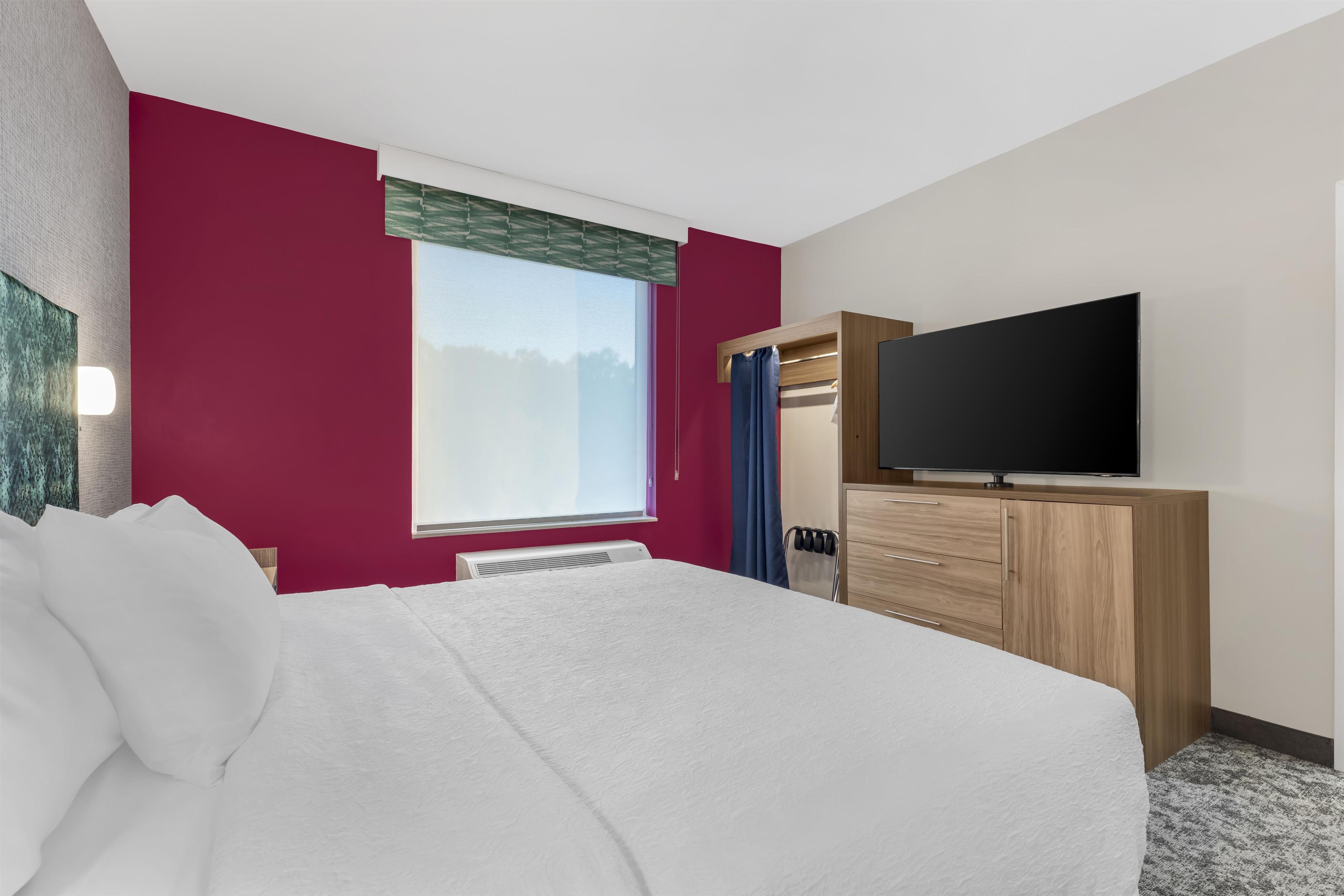 A hotel room with a bed, a television, a wardrobe, and a window.