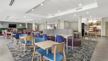 A modern dining area with multiple tables and chairs, a snack bar, and a large flat-screen TV.