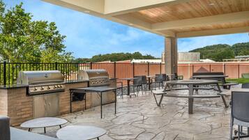 An outdoor patio with a grill, tables, and chairs.