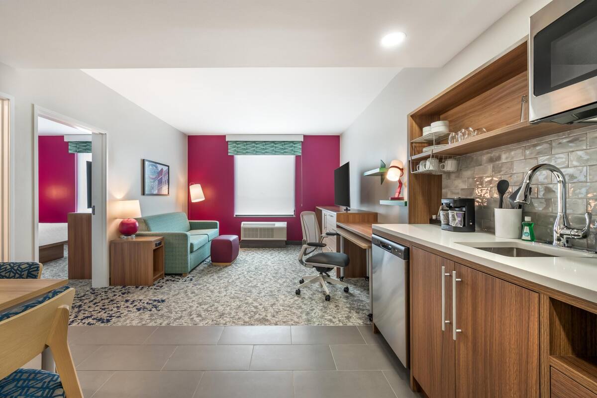 Een ruimtelijk ingerichte leefruimte met een kitchenette, een eethoek en een zithoek met een bank en een lamp.