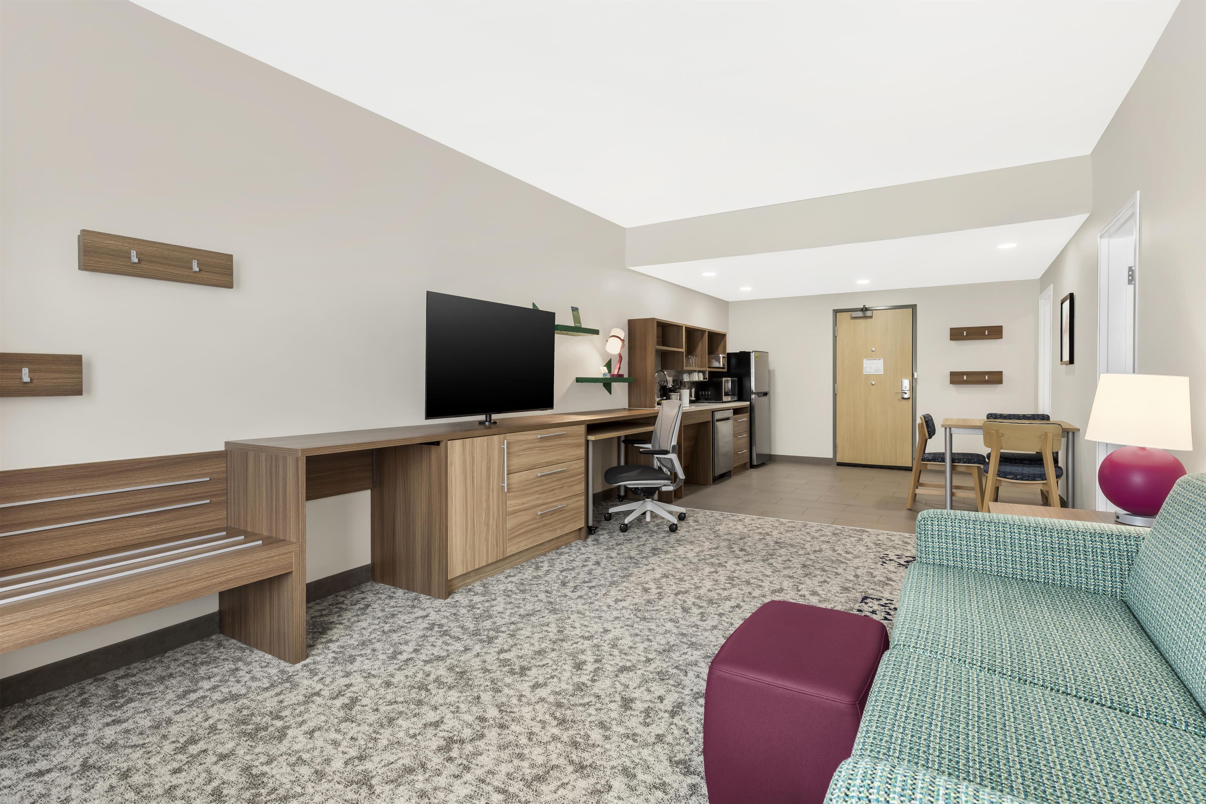 A modern living room with a wooden desk, a flat-screen TV, a sofa, and a dining area with a table and chairs.