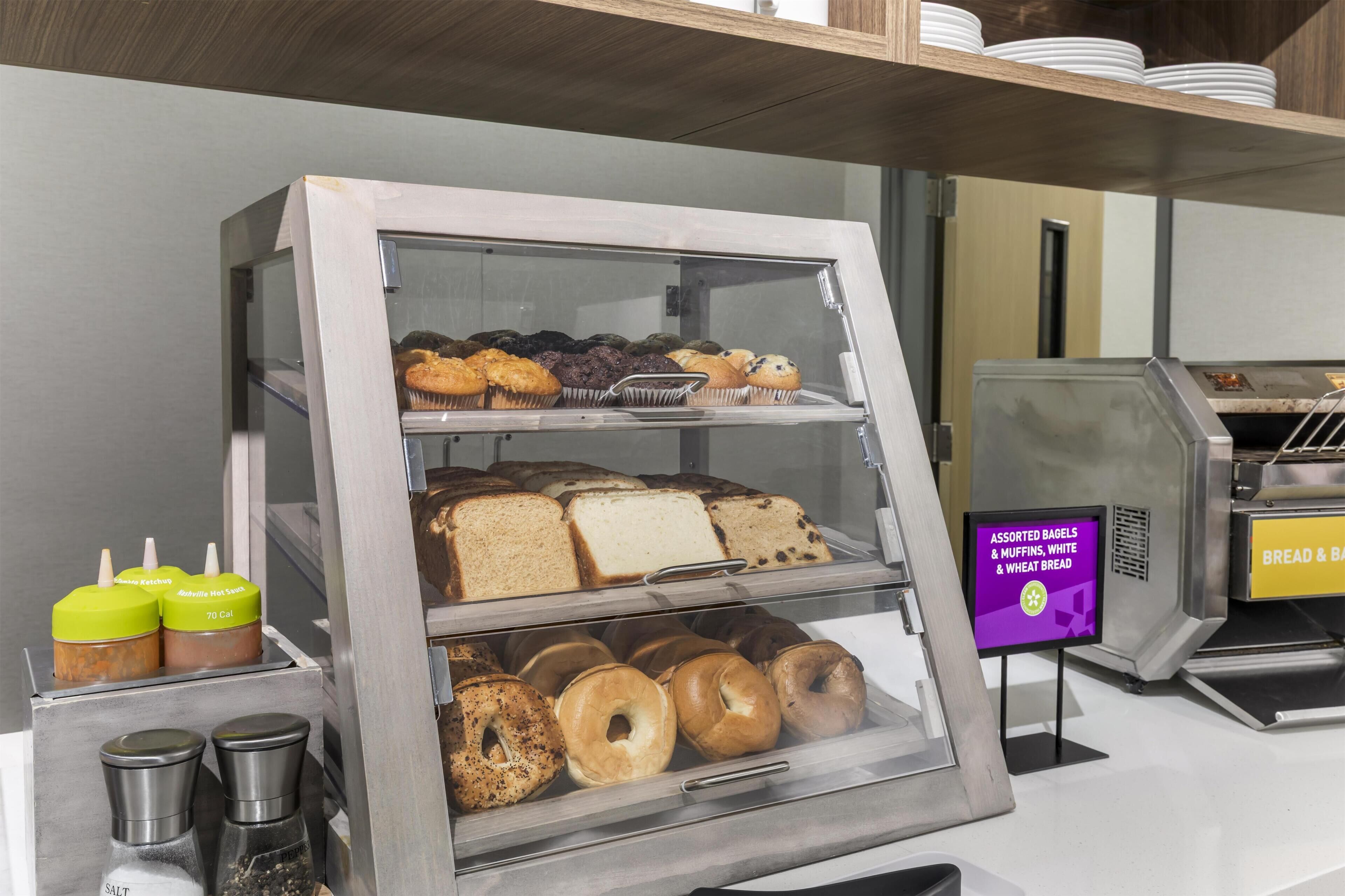 A bakery display case with assorted bagels, muffins, and bread.