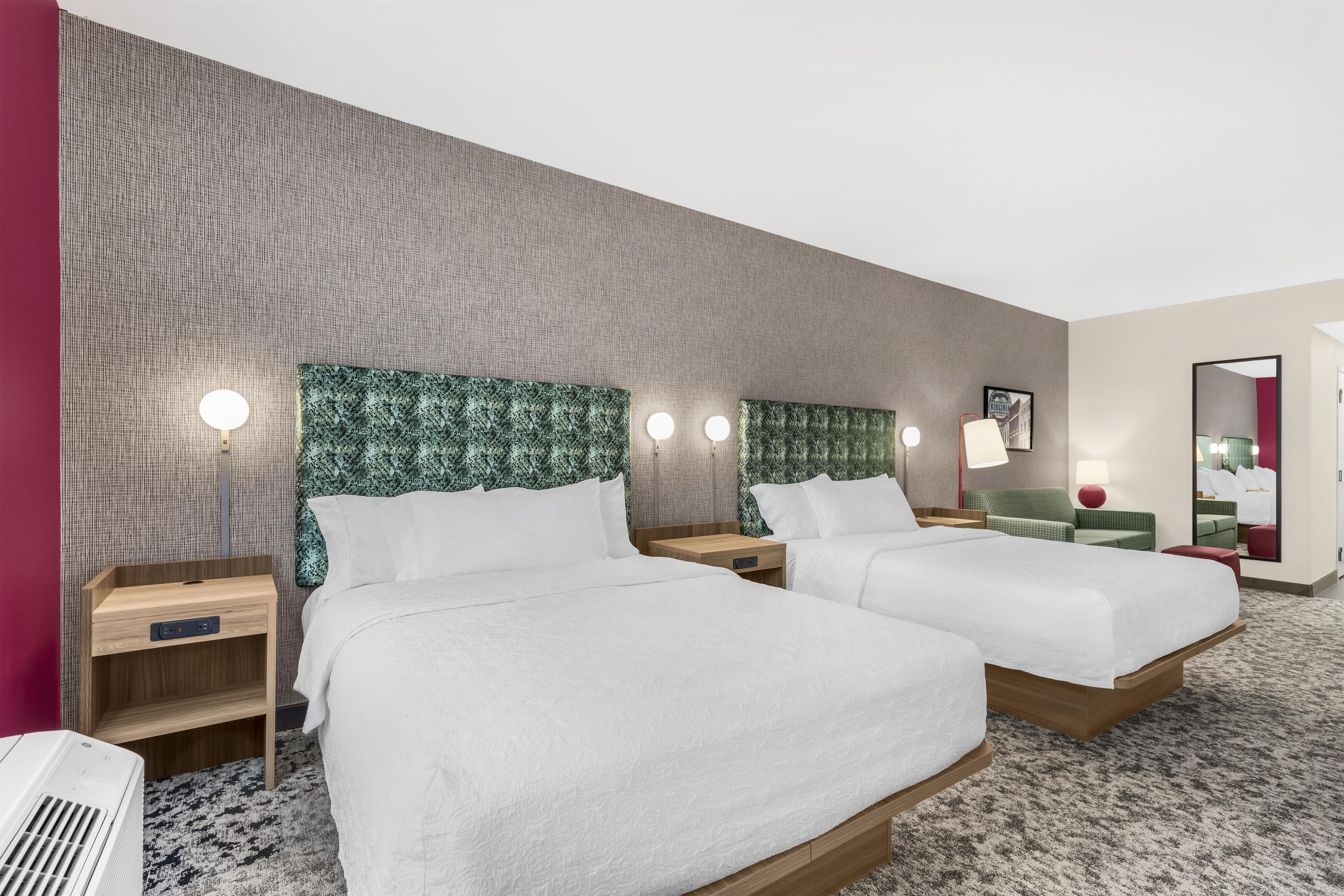 Une chambre d’hôtel avec deux lits, un grand miroir et un mur orné d’un motif texturé.