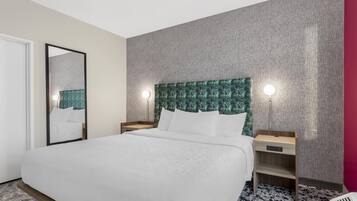 Habitación de hotel con una cama grande, una mesita de noche, un espejo y una pared con textura.