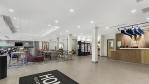 Un hall d’hôtel comprenant un comptoir d’accueil, un espace salon et un grand tapis orné du mot « HOME ».