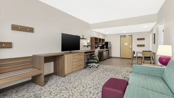 A modern living room with a wooden desk, a flat-screen TV, a sofa, and a dining area with a table and chairs.