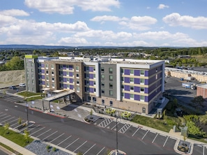 A multi-story hotel with a parking lot and a view of distant mountains. - Home2 Suites By Hilton Harrisonburg University (Harrisonburg)