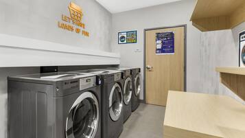 A laundry facility with multiple LG commercial washers, a wooden bench, and a sign indicating a front desk for stepping out.