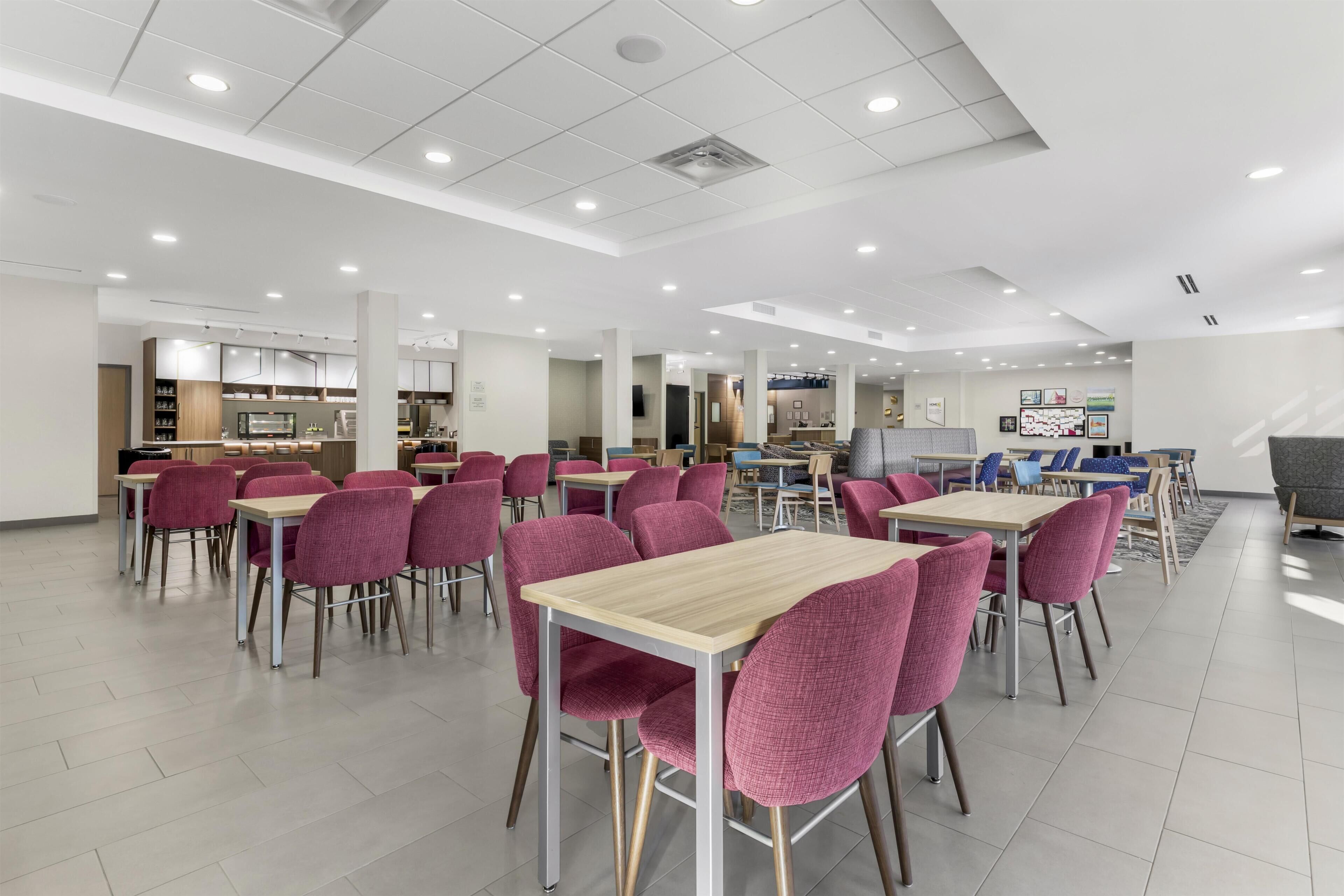 A spacious cafeteria with multiple tables and chairs, a counter with food display, and a seating area with a sofa and chairs.