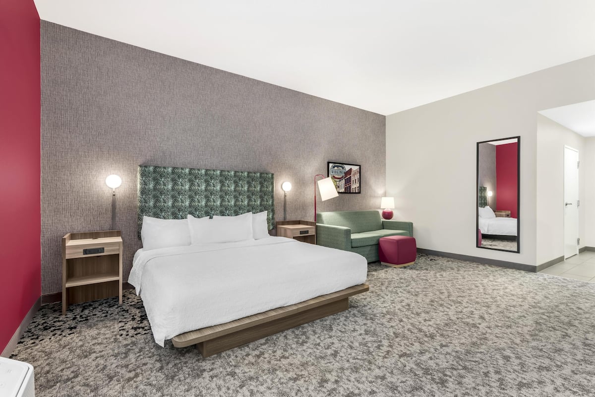 Een hotelkamer met een bed, nachtkastjes, een groen bekleden hoofdeinde, een rode accentmuur, een spiegel en een vloerbedekking.