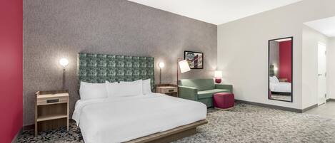 A hotel room with a bed, bedside tables, a green upholstered headboard, a red accent wall, a mirror, and a carpeted floor.