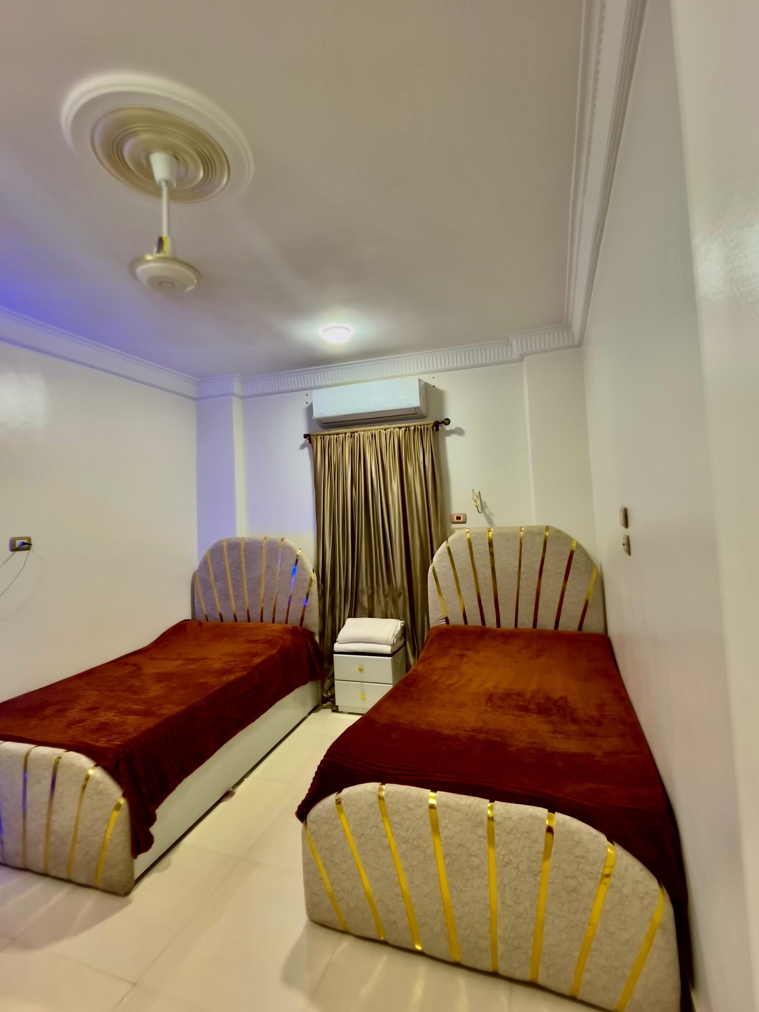 Ein Zimmer mit zwei Einzelbetten, einem Deckenventilator, einer Klimaanlage und einem kleinen Nachttisch mit Lampe.