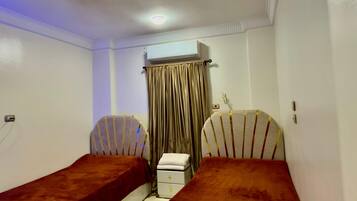 Ein Zimmer mit zwei Einzelbetten, einem Deckenventilator, einer Klimaanlage und einem kleinen Nachttisch mit Lampe.
