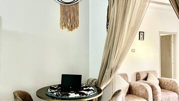 A modern living room with a round coffee table, a laptop, and a chandelier. There are plush chairs and a sofa with curtains.