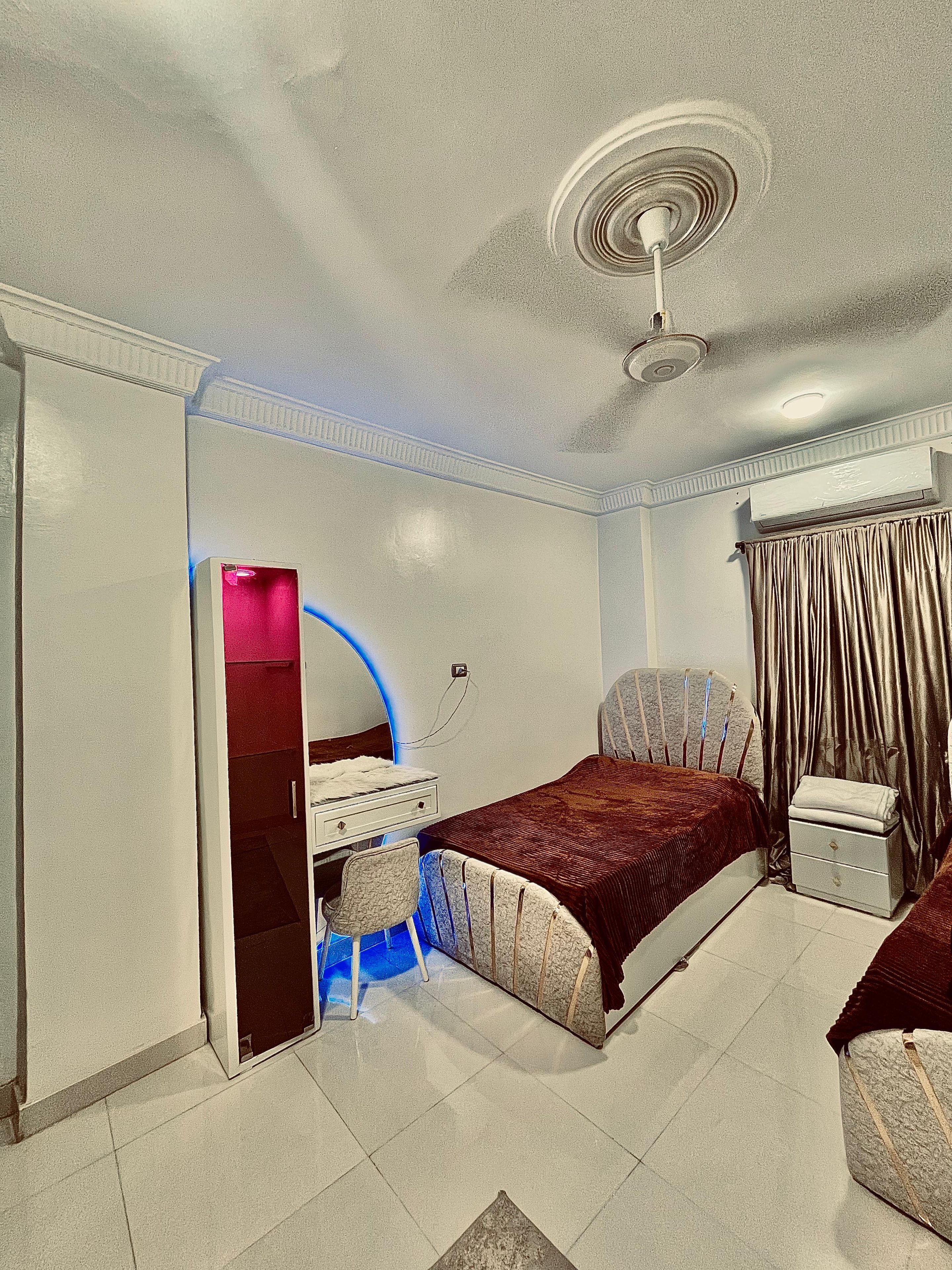 Quarto com cama, escrivaninha, cadeira e ventoinha no teto.