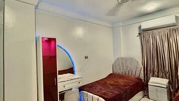 Quarto com cama, escrivaninha, cadeira e ventoinha no teto.
