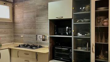 Eine moderne Küche mit Gasherd, Backofen und Mikrowelle. Ein Schrank mit Glastüren zeigt Geschirr.