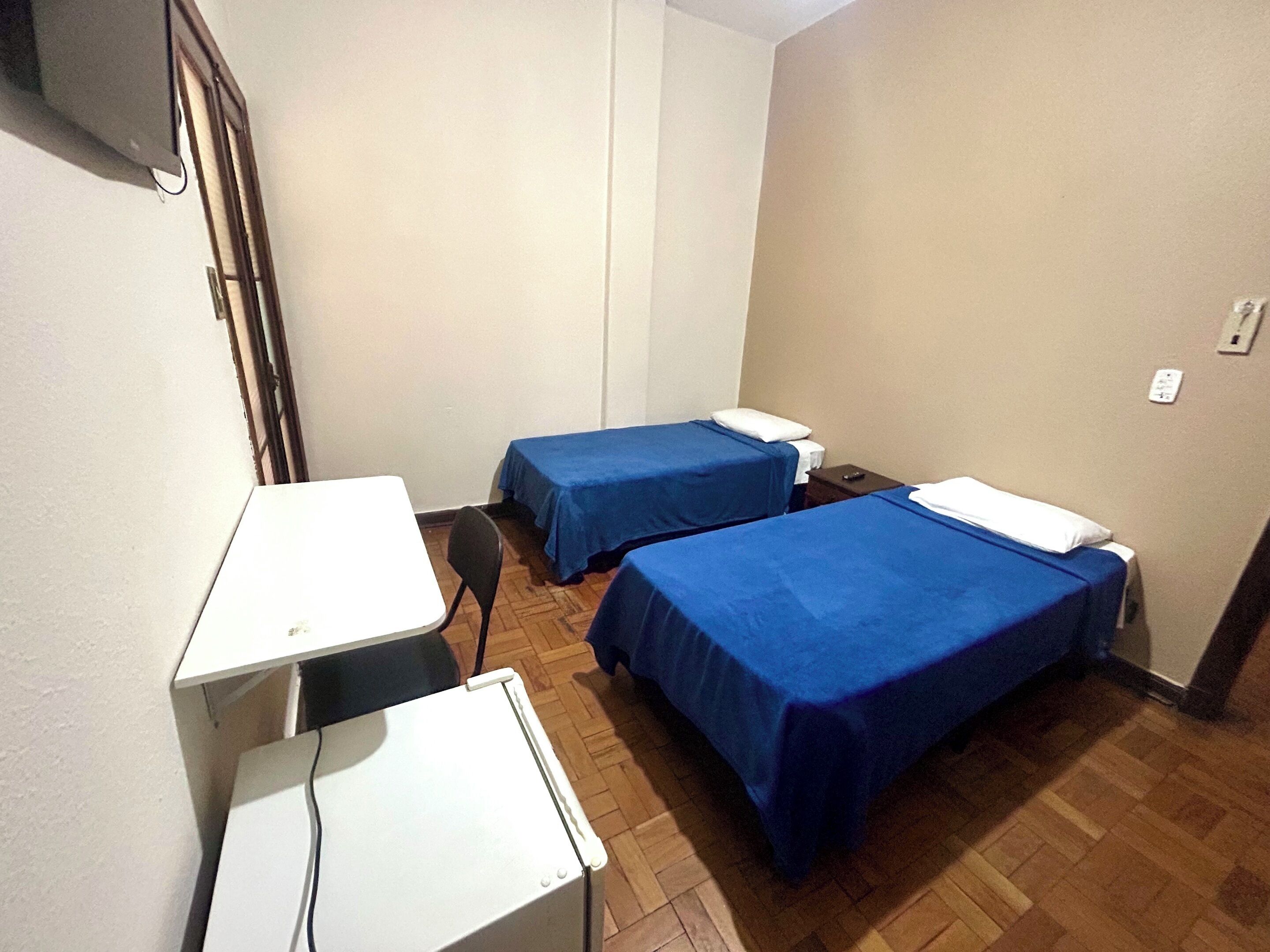 Ein kleines Zimmer mit zwei Betten, einem Schreibtisch und einem Stuhl.