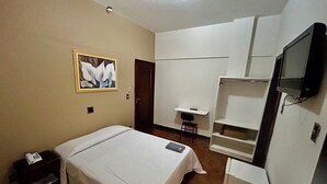 A bedroom with a bed, a desk, a chair, a TV, and a painting on the wall. - Hotel Jaú (Jau)
