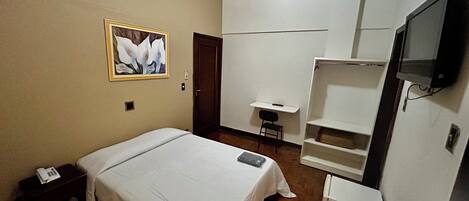 Un dormitorio con una cama, un escritorio, una silla, un televisor y un cuadro en la pared.