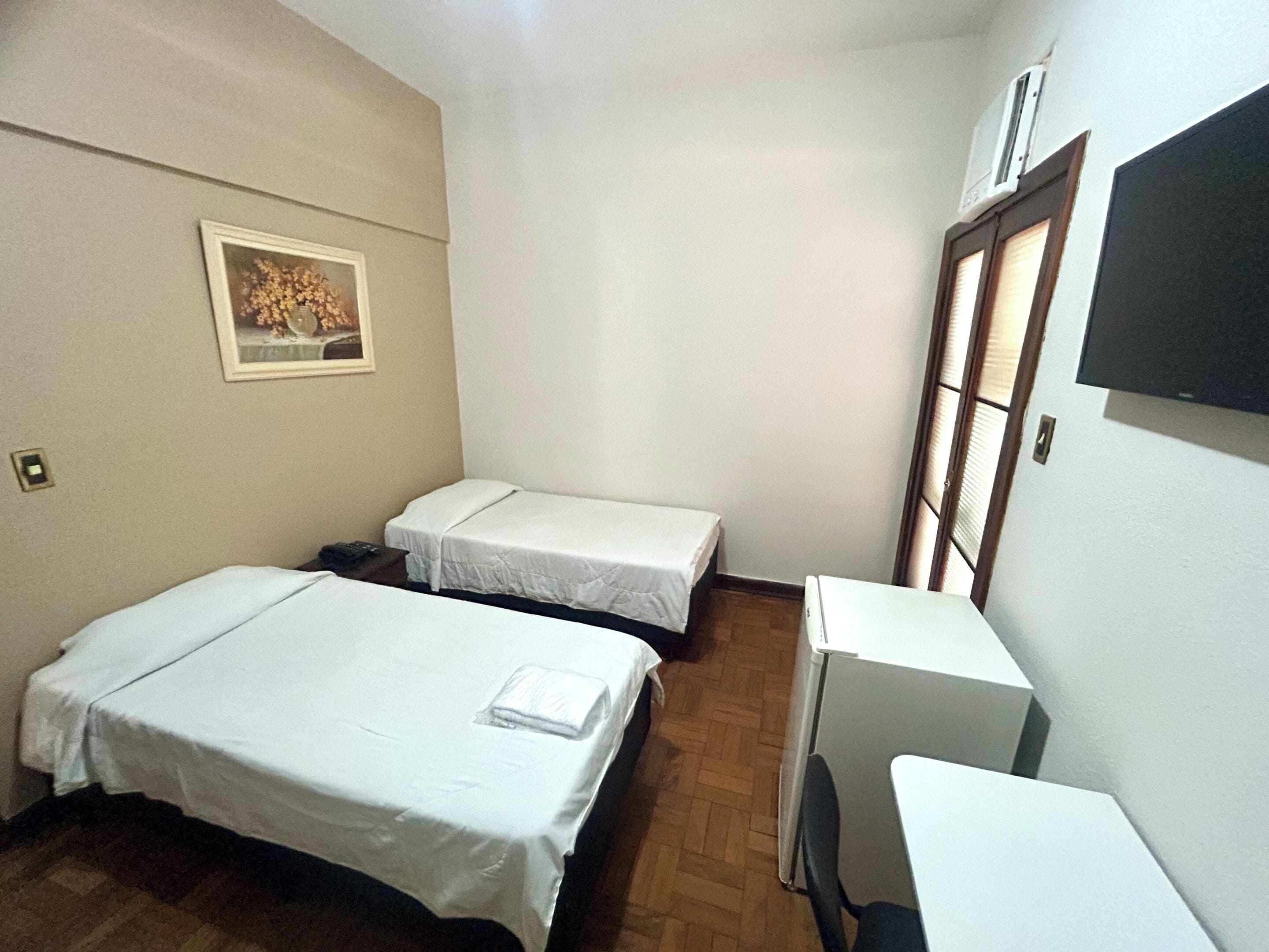 A small, clean room with two single beds, a desk, a chair, and a TV.
