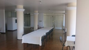 A large, open room with a long table and chairs, white columns, and a high ceiling. - Hotel Jaú (Jau)