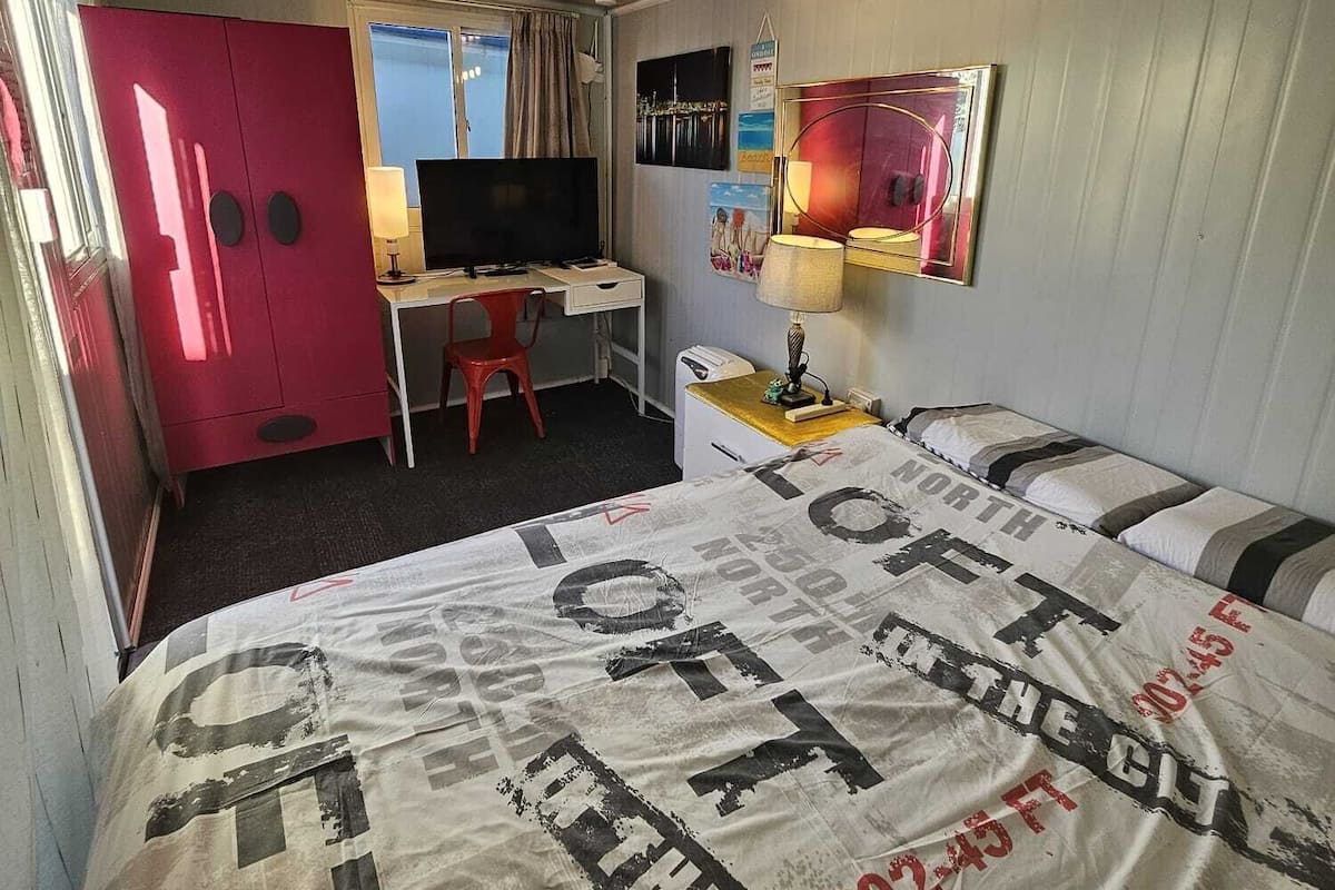 A compact hotel room with a bed, a desk, a television, a wardrobe, and a window.