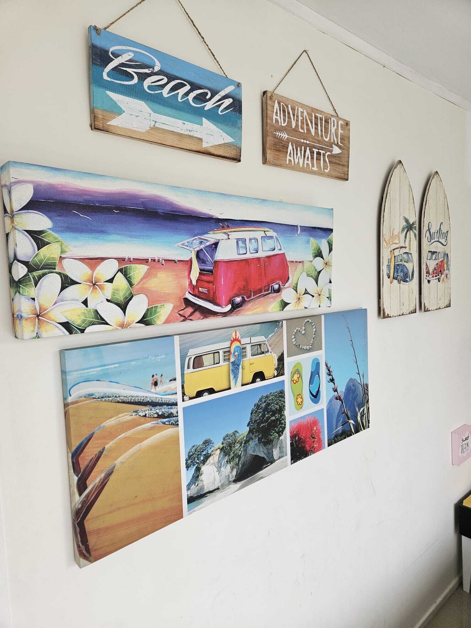 A wall with various travel-themed decorations including a beach sign, an adventure sign, and surfboards.