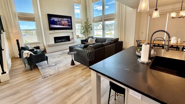 A modern living room with a large TV, comfortable seating, a fireplace, and a kitchen area with a sink and countertop. - Silicon Slopes Retreat (Lehi)
