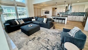 A modern living room with a sectional sofa, ottoman, and a small round table. - Silicon Slopes Retreat (Lehi)