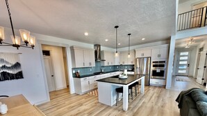 A modern kitchen with a central island, pendant lighting, and a view to the upper level. - Silicon Slopes Retreat (Lehi)