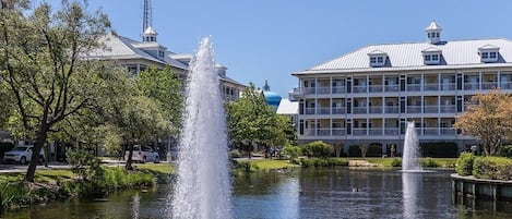 A hotel with a fountain in the courtyard, surrounded by trees and a body of water.