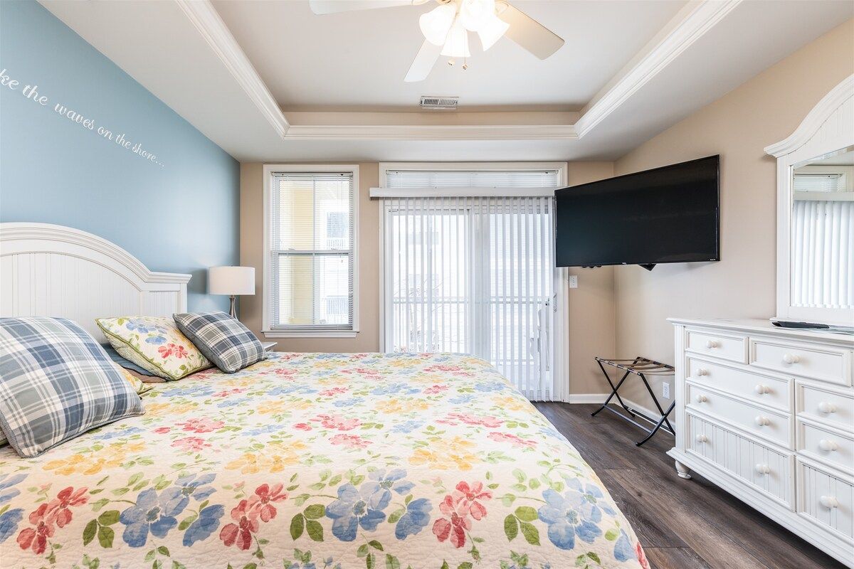 A bedroom with a bed, a dresser, a television, and a ceiling fan.