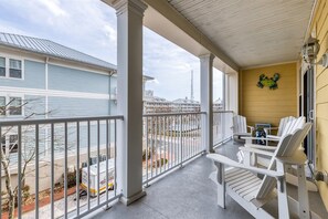 Een overdekt terras met witte Adirondack stoelen, een kleine tafel en decoratieve kikker wanddecoratie.