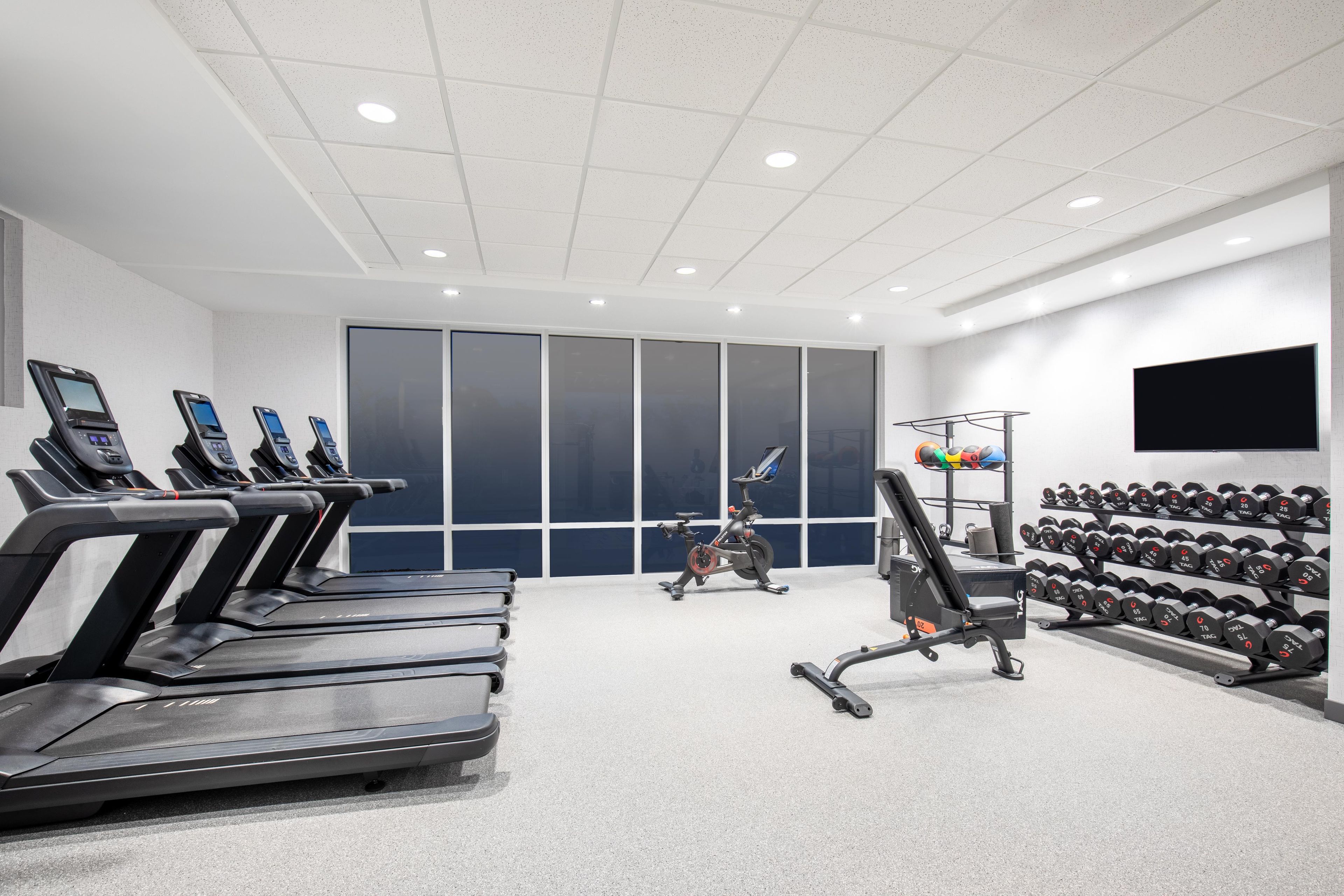Une salle de sport équipée de tapis de course, d’un vélo d’exercice et d’une série d’haltères.