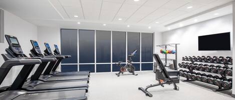 Un gimnasio con cintas de correr, una bicicleta estática y un soporte con mancuernas.