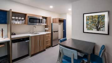 Cocina funcional con lavavajillas, microondas y refrigerador. Hay una mesa de comedor con sillas y un cuadro en la pared.