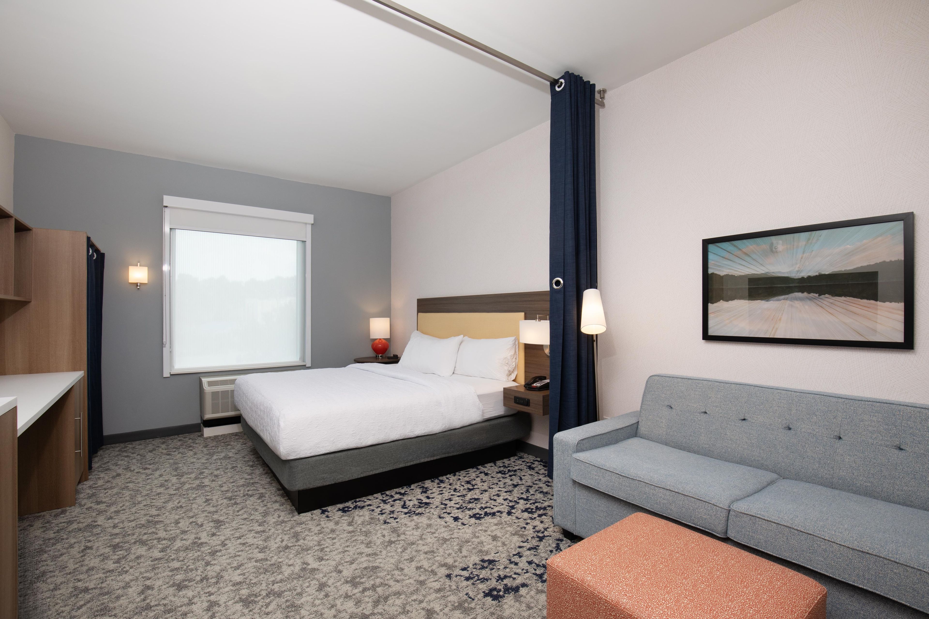 A hotel room with a bed, a sofa, a desk, and a painting on the wall.