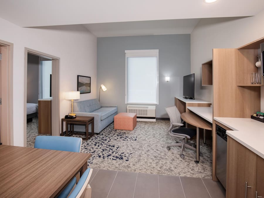 A compact hotel room with a kitchenette, a sofa, a dining table, and a TV.