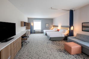 A hotel room with a bed, a desk, a television, a sofa, and a carpeted floor. - Home2 Suites By Hilton Hoover Birmingham (Birmingham)