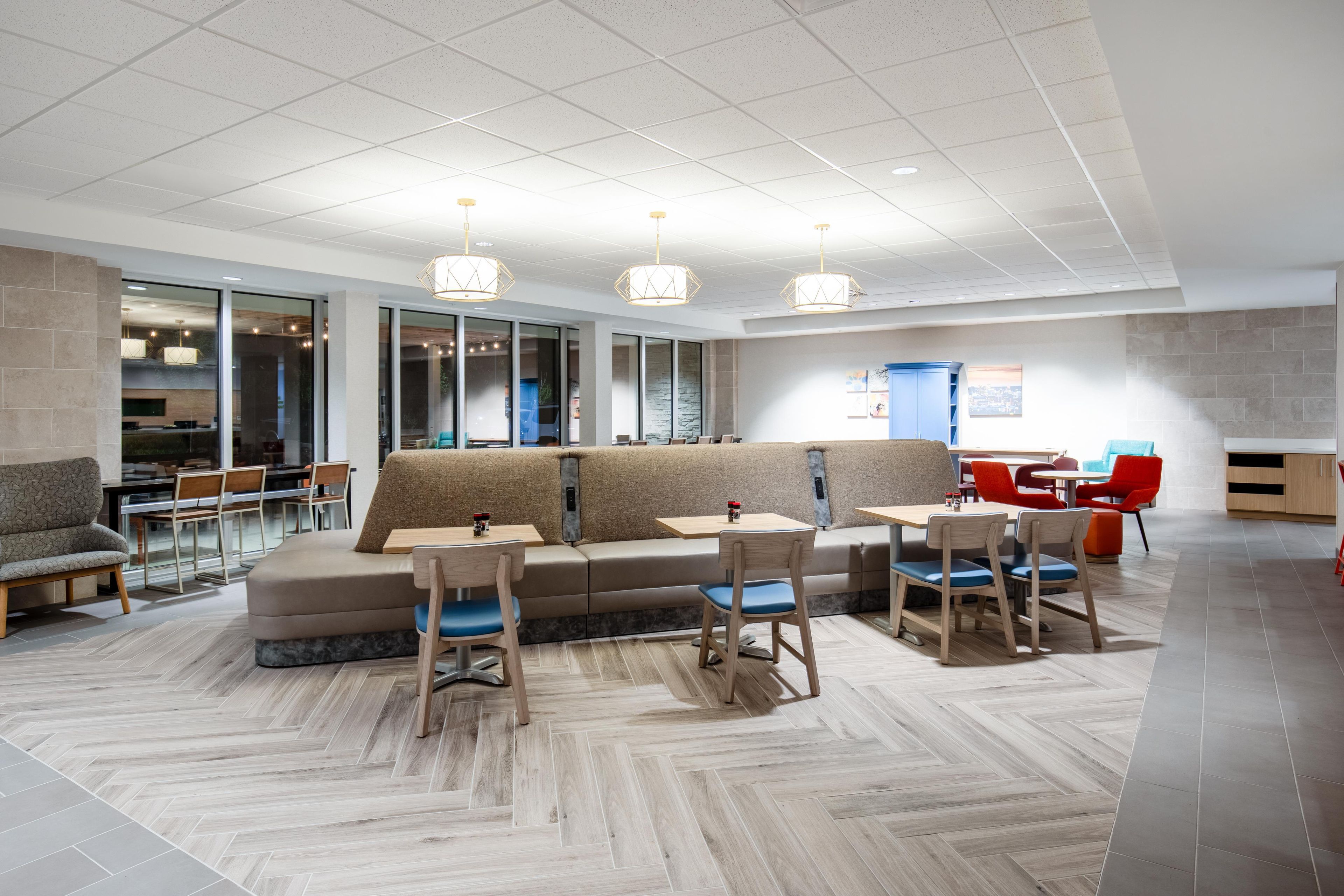 A modern interior with a seating area featuring sofas and tables, a kitchen area, and a view through large windows.