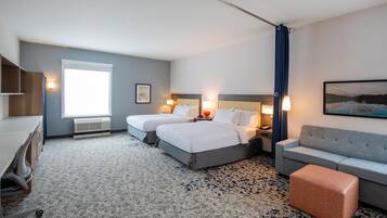 Habitación de hotel con dos camas, un escritorio, una silla, un sofá y un ventanal grande.