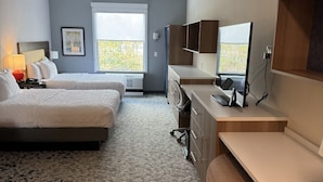 Een hotelkamer met twee bedden, een bureau, een stoel, een televisie en een raam met uitzicht.