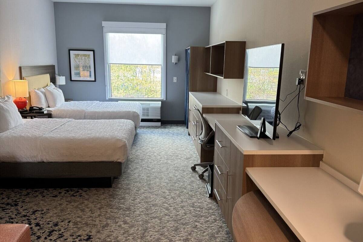 Een hotelkamer met twee bedden, een bureau, een stoel, een televisie en een raam met uitzicht.