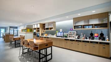 Un área de cocina moderna con una isla central, taburetes de bar y una encimera con distintos alimentos y electrodomésticos.