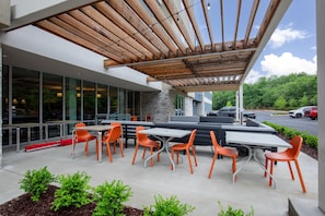 An outdoor seating area with tables and chairs, a covered patio, and a view of the street. - Home2 Suites By Hilton Hoover Birmingham (Birmingham)