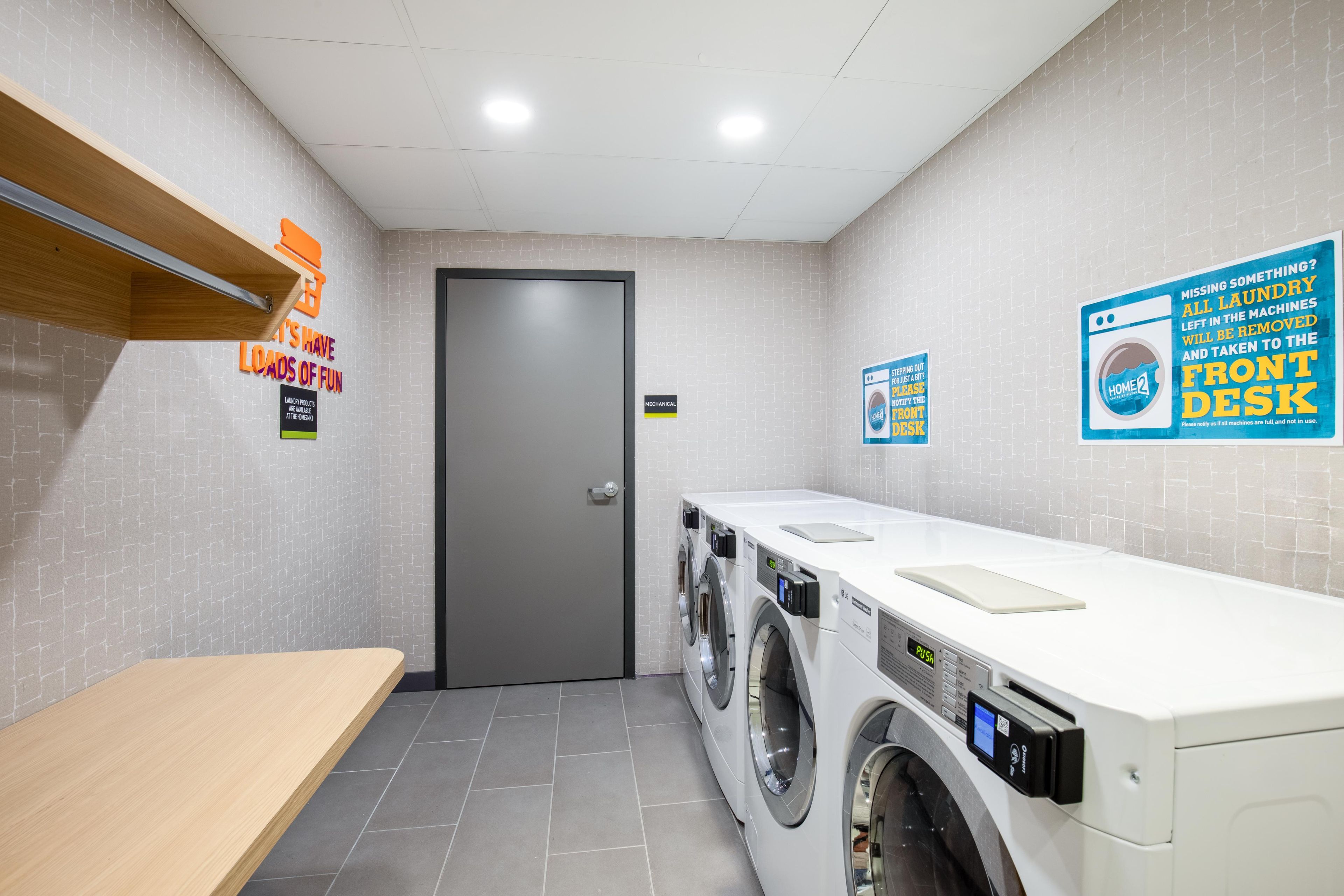 A laundry facility with a grey door, a wooden shelf, and multiple washing machines.